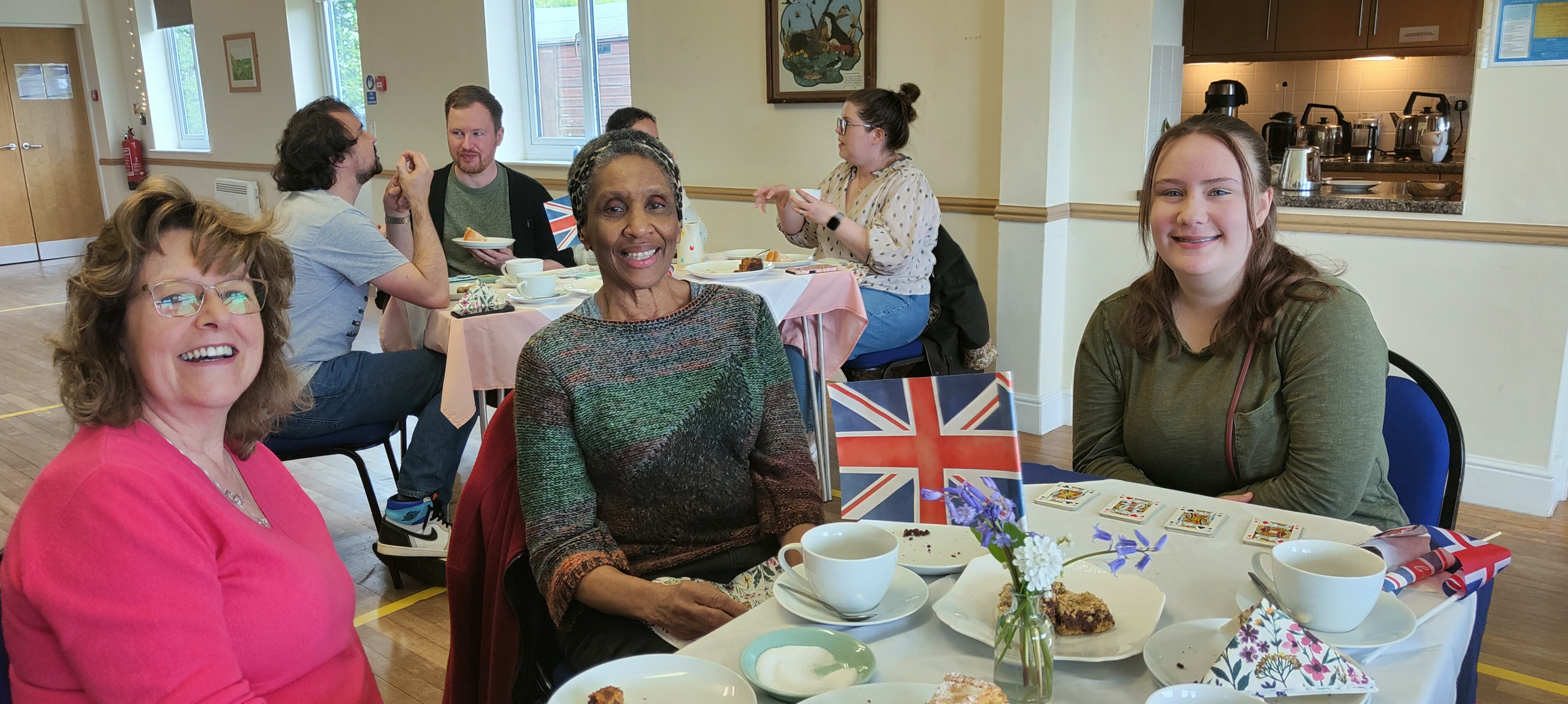 People smiling and laughing sitting around tables enjoying coffee and cake